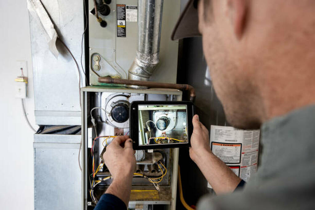 Young Male Property Inspector Photographing a Furnace Hot Water Heater and Air Conditioning Unit Inside a Residential Home Garage