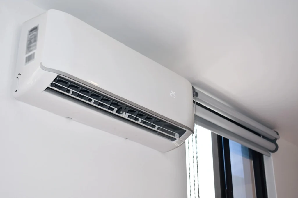 A white ductless mini-split air conditioner indoor unit mounted on a wall near a window.