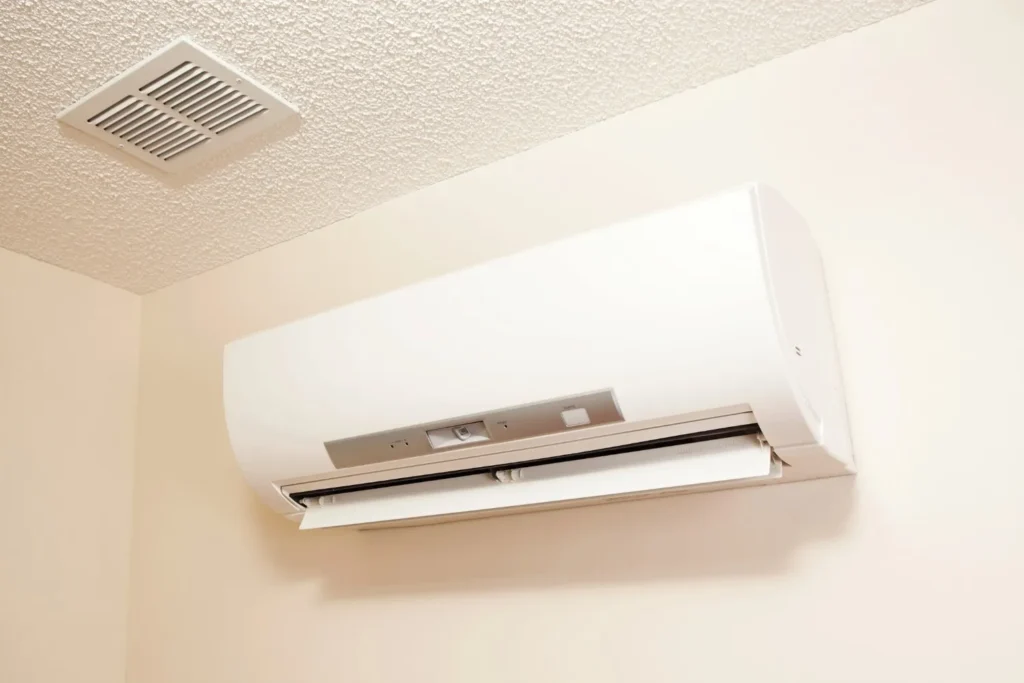 A white ductless mini-split air conditioner indoor unit mounted high on a wall below a ceiling vent.