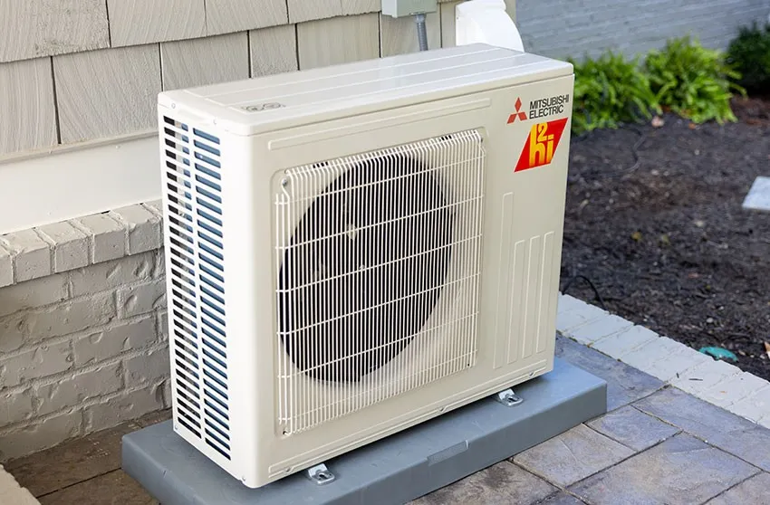 An outdoor Mitsubishi Electric heat pump unit resting on a gray pad next to a house wall.